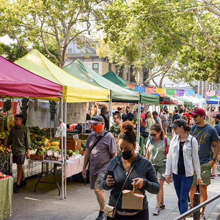 Busy outdoor farmers market with colorful vendor tents and shoppers