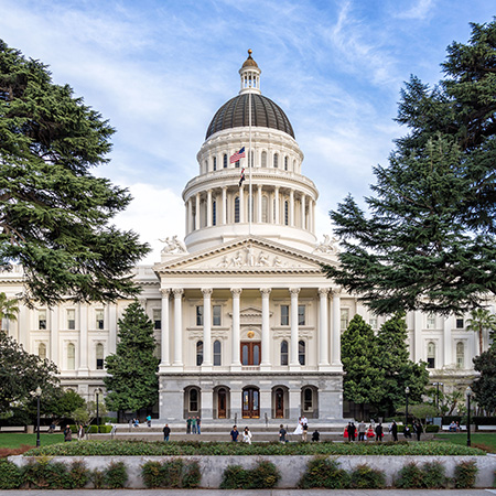 Sacramento capitol with central dome, front portico, trees and blue sky