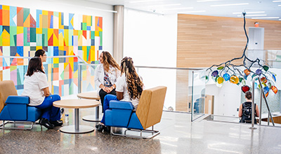 People chatting on blue chairs in a bright lounge with colorful geometric wall art.