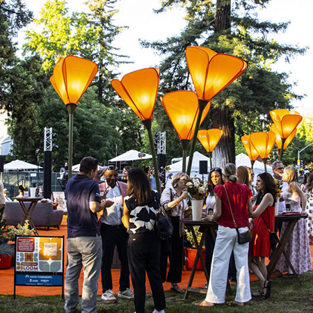 Evening outdoor festival with people gathered under tall glowing orange tulip-shaped lamps