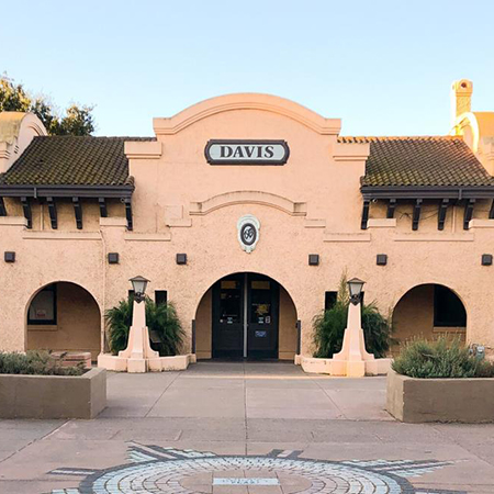 Spanish-style beige building labeled "Davis" with arched doorways, small statues and tiled foreground